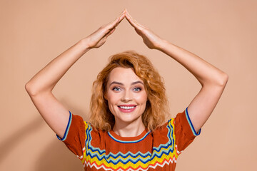 Portrait of good mood funky girl with ginger hairdo wear knit t-shirt palms show roof over head isolated on beige color background