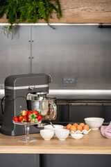 A modern kitchen setting featuring a professional stand mixer with ingredients like fresh strawberries in a glass, eggs, and bowls of flour, ready for a baking session,.