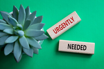 Urgently needed symbol. Concept word Urgently needed on wooden blocks. Beautiful green background...