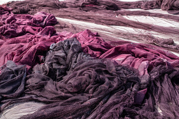 A detailed view of discarded maroon and white fishing nets piled on a dock, symbolizing...
