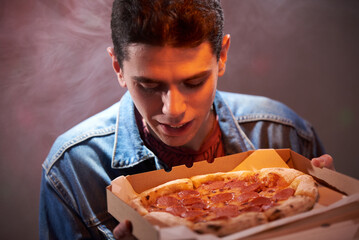 Young happy guy with pepperoni pizza in a cardboard box