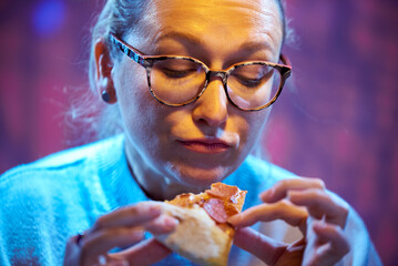 Hungry adult woman in glasses eating pizza with pleasure