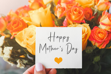 bright bouquet of orange yellow roses and white cardboard card with the inscription text happy mothers day and orange heart