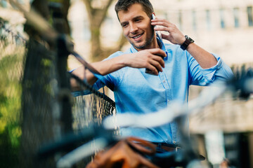 Smiling businessman using smartphone while leaning on bicycle in urban setting