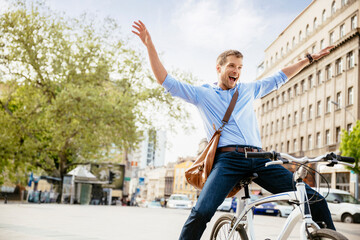 Happy businessman riding bicycle in city with arms raised