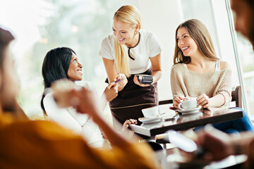 Smiling waitress taking payment from customers at coffee shop