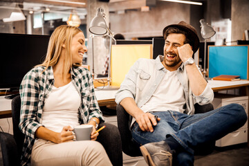 Two young professionals laughing and relaxing with coffee during office break