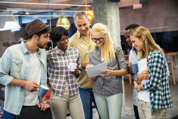 Diverse team of professionals discussing project with coffee in modern office