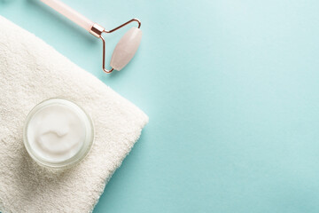 Skin care products. Cream jar, jade roller and white towel on blue background. Flat lay with copy...