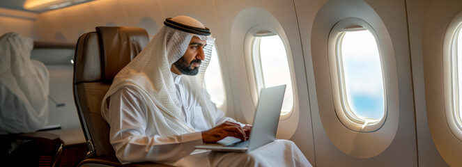 Islamic entrepreneur in cultural dress multitasking on laptop at 30,000 feet during work journey