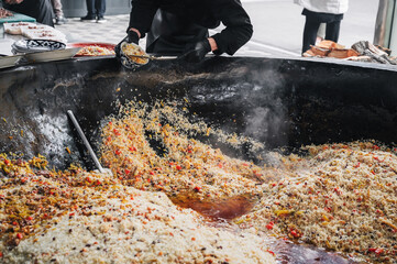 male cook puts cooked Uzbek pilaf from a cauldron on a plate. Traditional Oriental Arabic rice cuisine. Central Asian Pilaf Center Besh Qozon in Uzbekistan in Tashkent