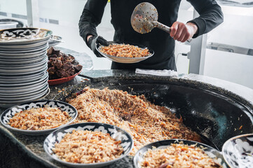 male hands chef cooking traditional oriental Arabic Uzbek pilaf with meat in a cauldron. Central Asian Pilaf Center in Uzbekistan in Tashkent