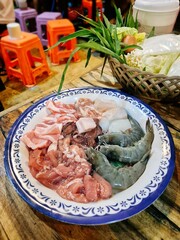 Thai barbecue grilling pork on a hot pan. Plate of raw meats and seafood, prepared for cooking. Thai street food.