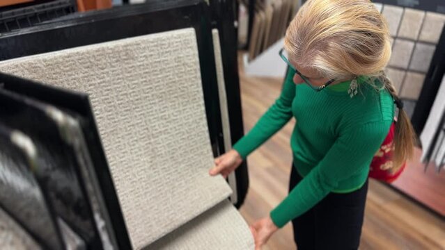 Mature woman looking at carpet samples shopping looking rug for home redecorating project, in a hardware store.