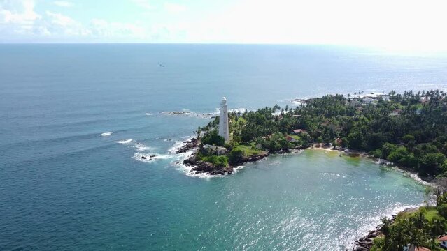 White colonial Dondra Head lighthouse surrounded by the ocean and palms on the jungle coast of Sri Lanka