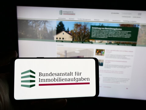 Stuttgart, Germany - 04-15-2024: Person holding smartphone with logo of German agency Bundesanstalt f&uuml;r Immobilienaufgaben (BImA) in front of website. Focus on phone display.
