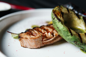 Grilled salmon fish fillet with vegetables and avocado on the plate, close up