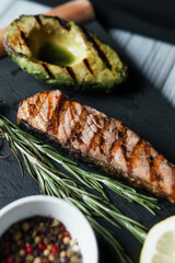 Grilled salmon fish fillet with green salad on the black cutting board, close up