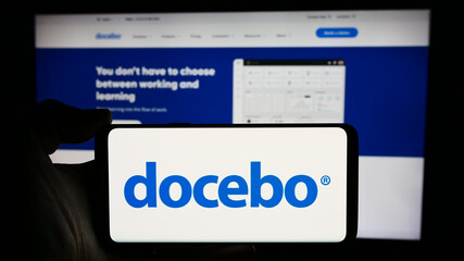Naklejka premium Stuttgart, Germany - 04-17-2024: Person holding cellphone with logo of Canadian learning software company Docebo Inc. in front of business webpage. Focus on phone display.