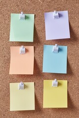 Six blank pastel-colored post-it notes are pinned neatly to a brown cork board
