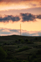 Electric pole on top of a hill with vibrant orange light in the background during sunrise.