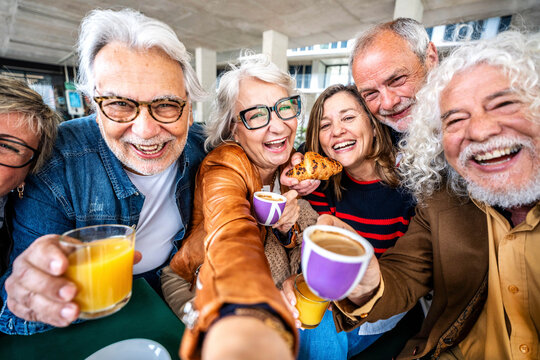 Happy senior people taking selfie picture sitting at cafe bar table - Older friends having breakfast together drinking coffee and fruit juice outdoors - Food and beverage lifestyle concept - Powered by Adobe