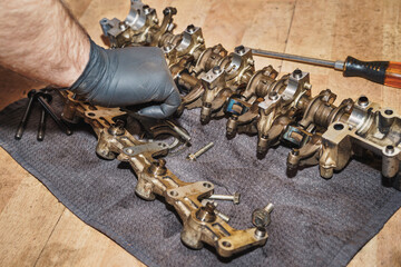 The auto mechanic cleans the rocker arm assembly, which is on the floor with screws and a screwdriver.