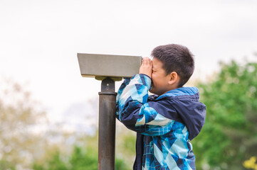 Boy looking in telescope in park. Tourists on observation deck.