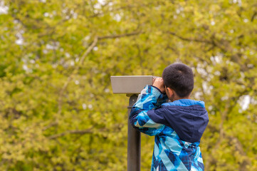 One boy looking in telescope in park. 