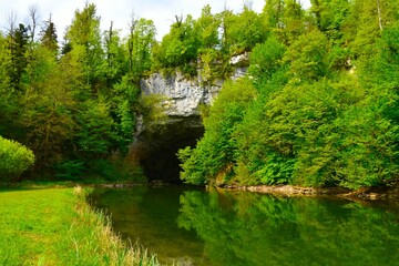 Big natural bridge and Rak river with a reflection in the water in Notranjska, Slovenia