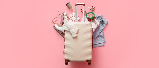 Suitcase with warm clothes, ice skates, Christmas deer horns and cup of coffee on pink background....