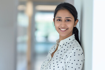 Professional young woman with a radiant smile poses at the office, showcasing confidence and positivity in a stylish polka-dot shirt, perfect for corporate and lifestyle imagery