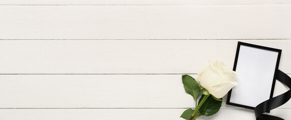 Rose with photo frame and black ribbon on white wooden background