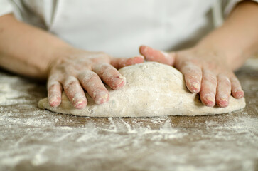 Fototapeta premium Handcrafting loaves of bread dough. Process occurs in a bakery. The dough is kneaded by warm hands.