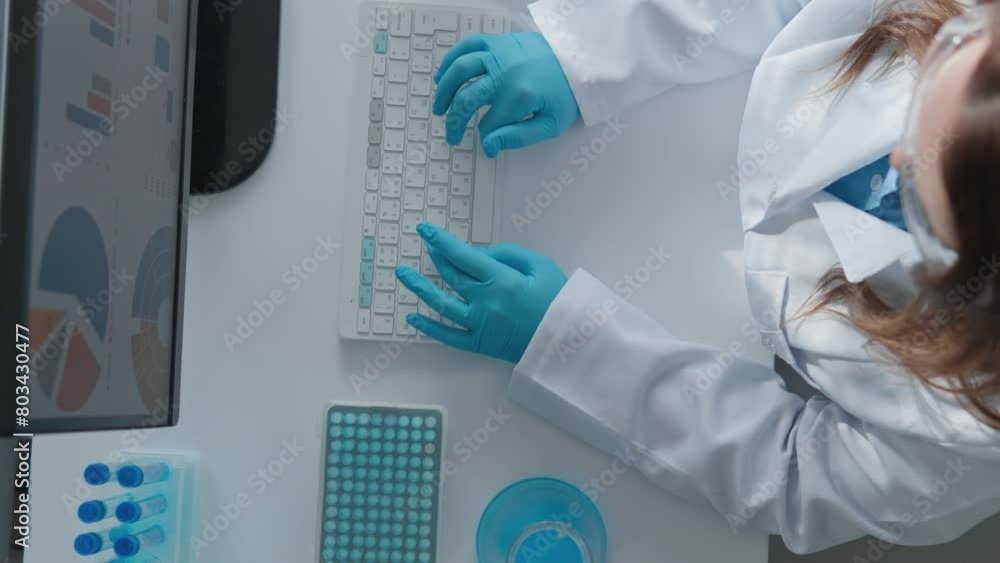 Poster Vaccine development in the laboratory. Technological modern laboratory of medical analyzes. Woman in white coat sitting at computer in protective gloves, typing on keyboard View from above.