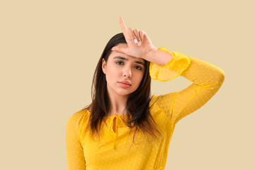 Upset young woman showing loser gesture on beige background, closeup