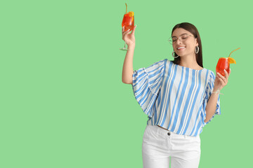 Beautiful young woman with glasses of tasty aperol spritz on green background