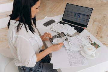 Side view of confident woman calculates utility expenses on laptop and calculator, engaged in...