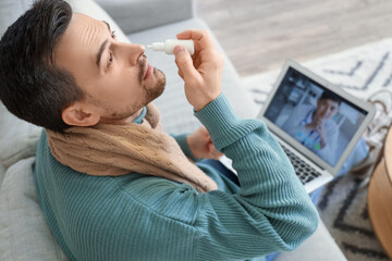 Ill young man using nasal drops while video chatting with doctor on laptop at home