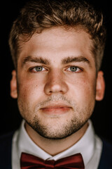 Valmiera, Latvia - August 19, 2023 - Close-up portrait of a young man with intense eyes and a slight beard, wearing a dark suit and red bow tie.