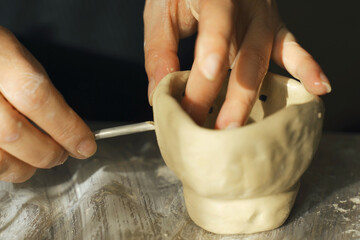 A woman makes holes using a tool in a clay craft - a candlestick.