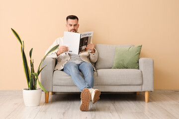 Handsome man reading magazine on sofa near beige wall