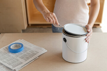 Woman opening a paint can. Using can opener to pry open the lid