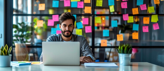 Businessman works on laptop computer with colorful sticky notes on a white wall to organize their Ideas on background, Data analysis and creative design, Startup Project. 