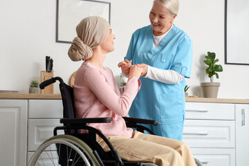 Fototapeta premium Young woman after chemotherapy in wheelchair with nurse holding hands at home. Stomach cancer concept