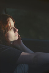 Close up shot of a pensive young woman with red hair driving a car while a beam of soft light...
