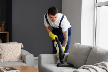 Male janitor cleaning sofa in room