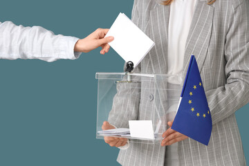 Hand putting voting paper into ballot box on blue background. Election concept