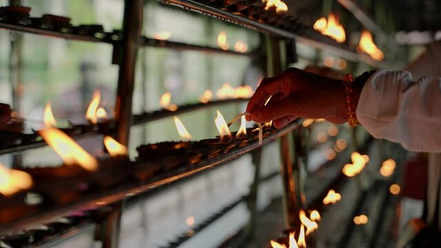 Person lights oil lamps for religious ritual in Buddhist temple. Devotees perform traditional offerings in sacred sanctuary. Flames flicker at spiritual ceremony. Worshipers seek blessings, meditate.