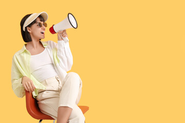 Young woman with megaphone sitting on chair against yellow background